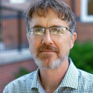 Man with short gray and brown hair wearing thin-rimmed glasses